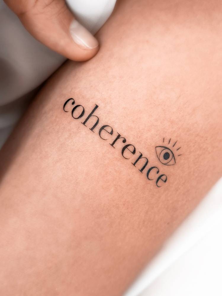 Word "coherence" and evil eye tattoo located on the inner forearm.