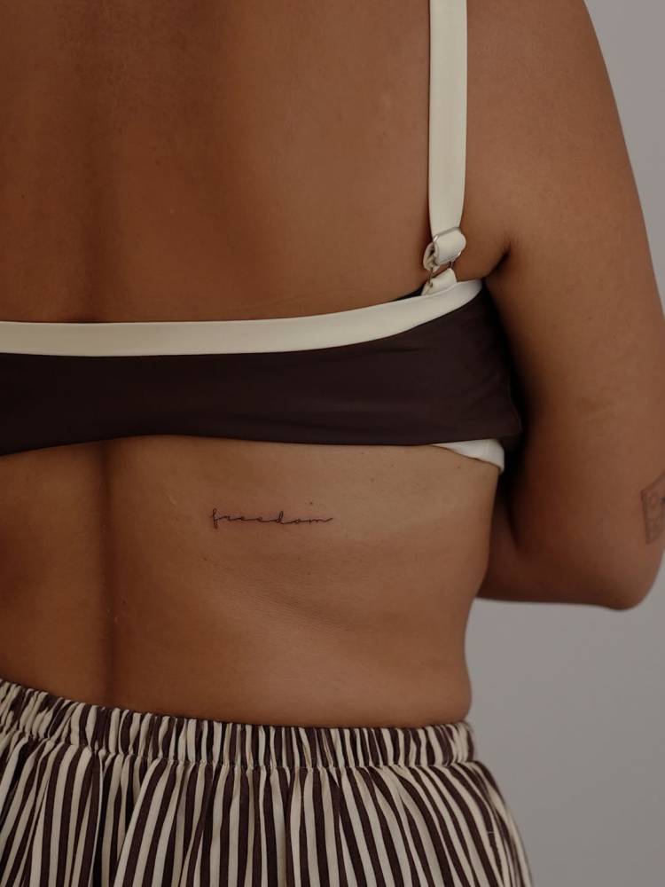 Handwritten font word "freedom" tattooed on the back.