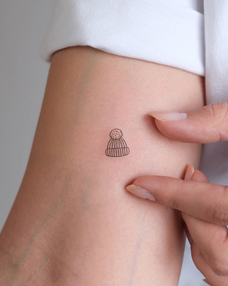 Knit cap tattoo in fine line style located on the inner arm.