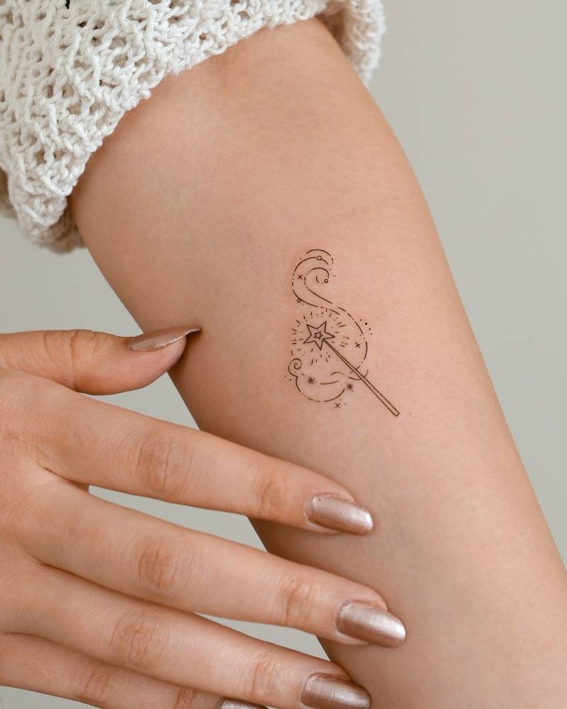 Magic wand tattoo in fine line style placed on the inner forearm.