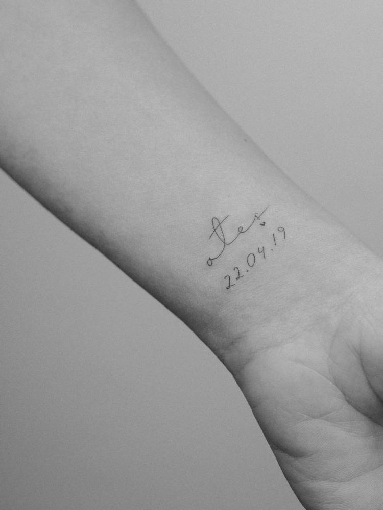 Lettering tattoo of the name "Ates" and birthdate located on the wrist.