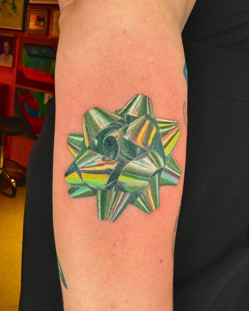 Metallic ribbon tattoo located on the forearm.