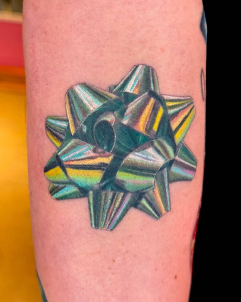 Metallic ribbon tattoo located on the upper arm.