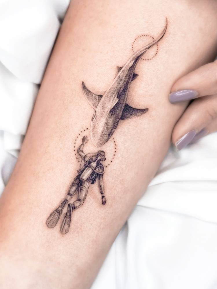 Micro-realistic style diver and shark tattoo located on the inner forearm.