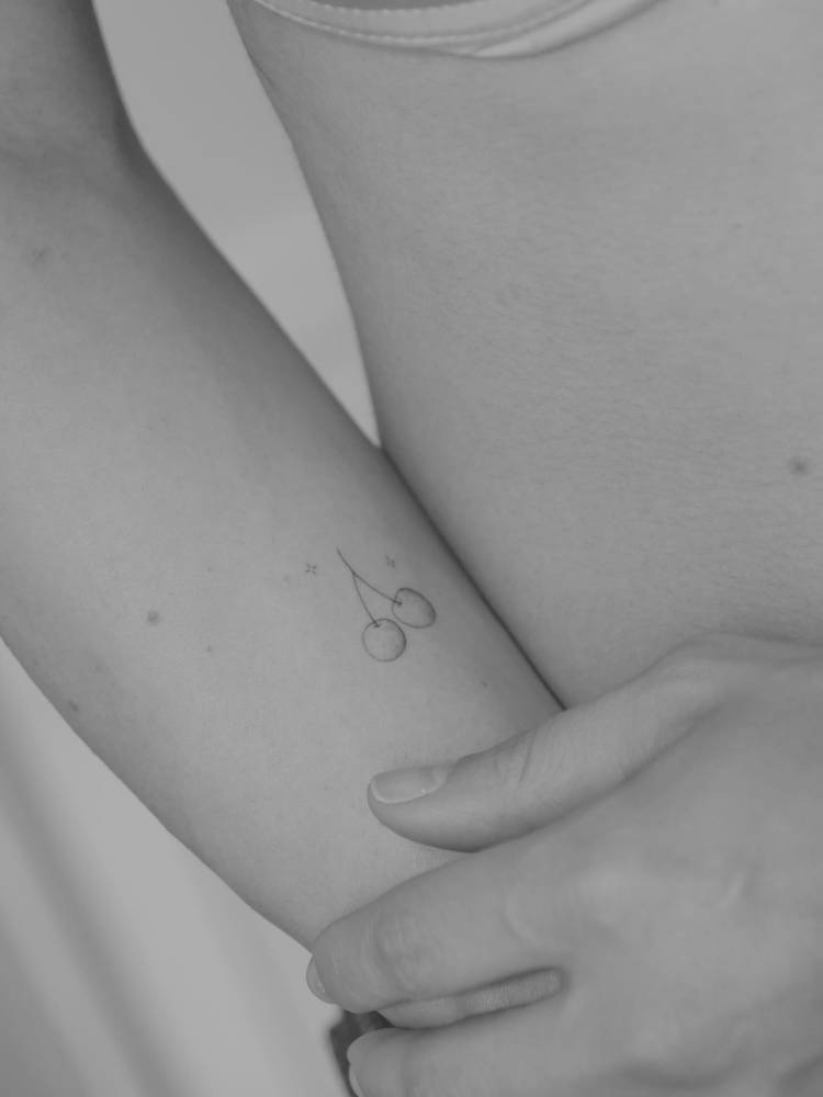 Fine line style cherries tattooed on the inner forearm.