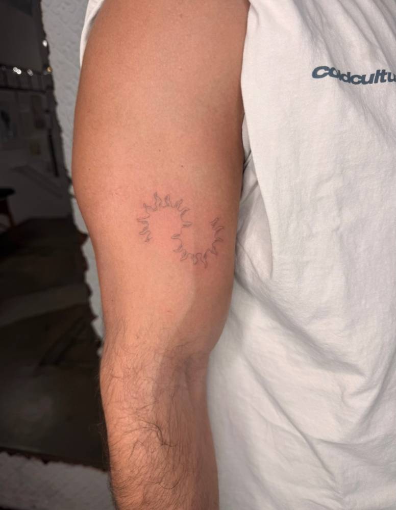 Two suns tattoo located on the upper arm, fine line style.