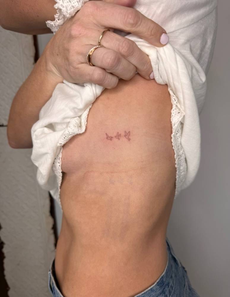 Tiny minimalistic flying birds tattoo placed on the side boob.