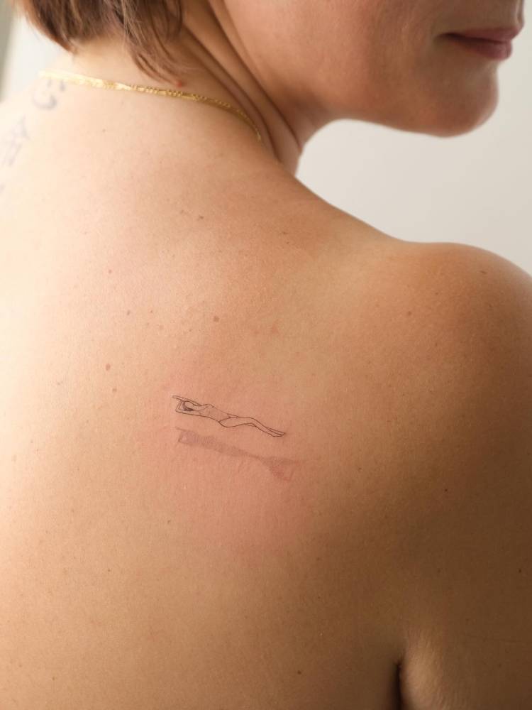 Swimmer tattoo in fine line style located on the shoulder blade.