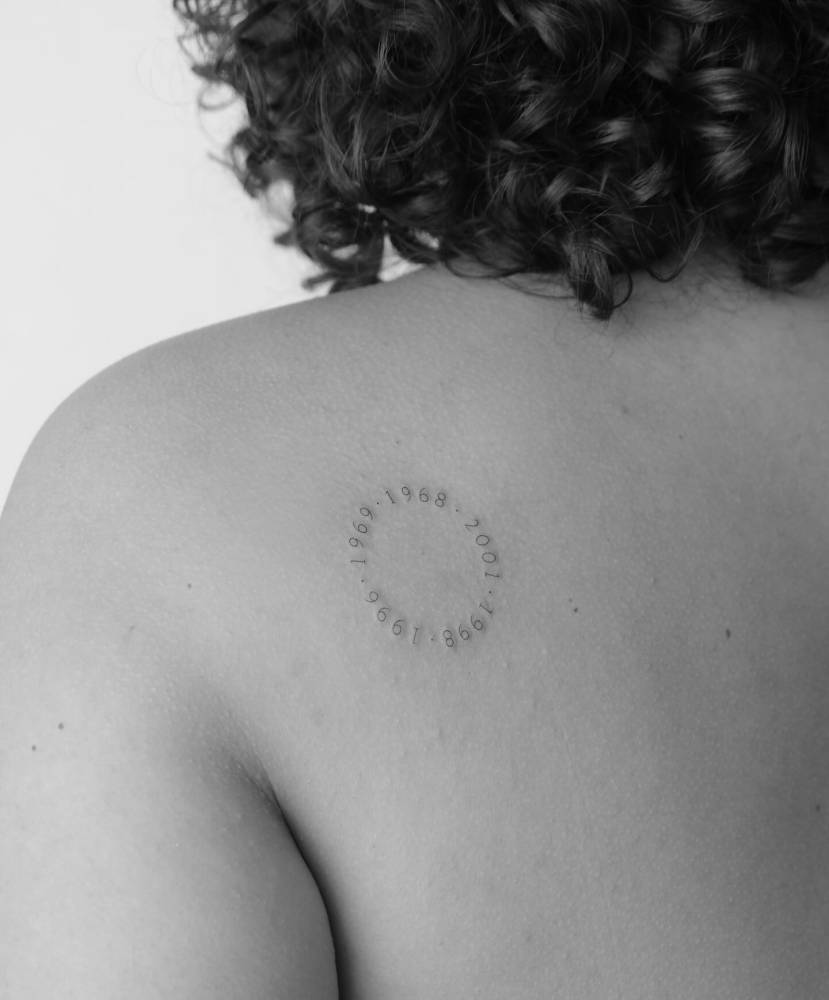 Family birth years circle tattooed on the shoulder blade.