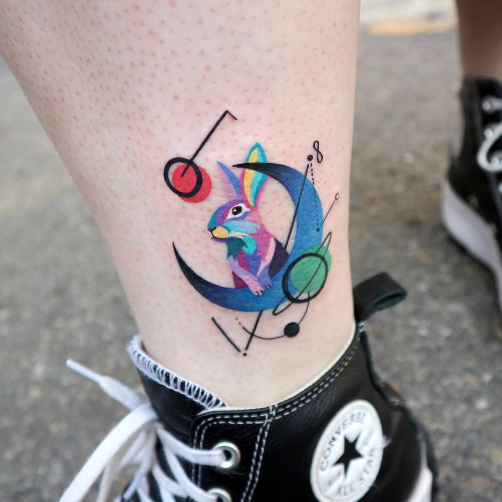 Graphic style rabbit and crescent moon tattoo located on the ankle.