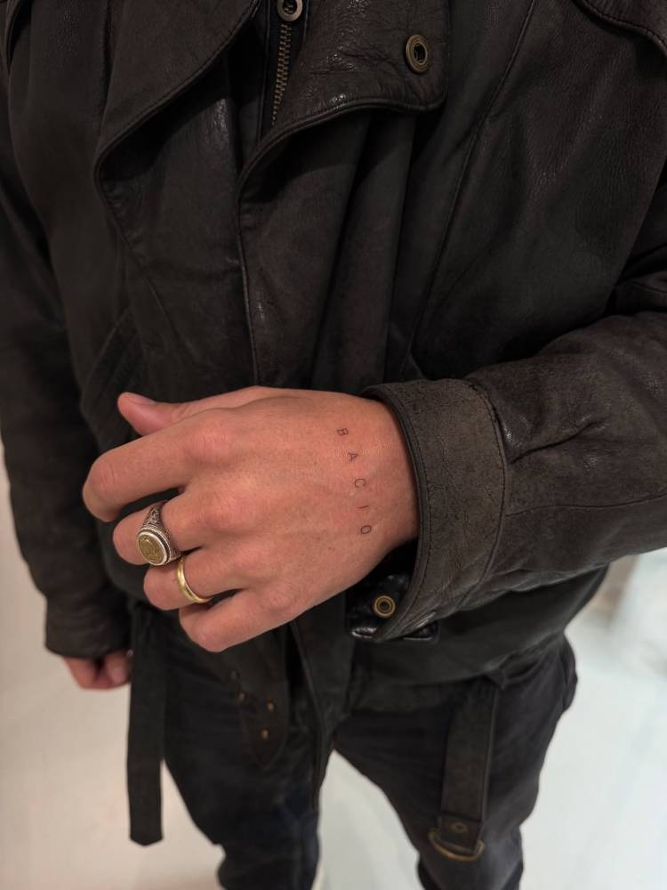 Word "bacio" lettering tattoo located on the hand.