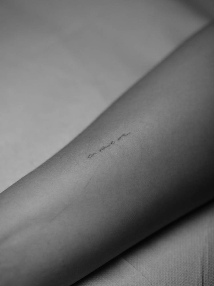 Handwritten font word "amore" tattooed on the wrist.