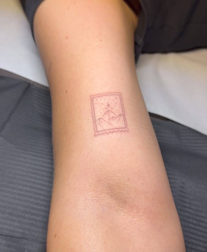 Fine line style mountain stamp tattoo placed on the bicep.