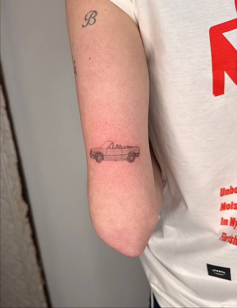 Car tattoo located on the tricep, illustrative style.