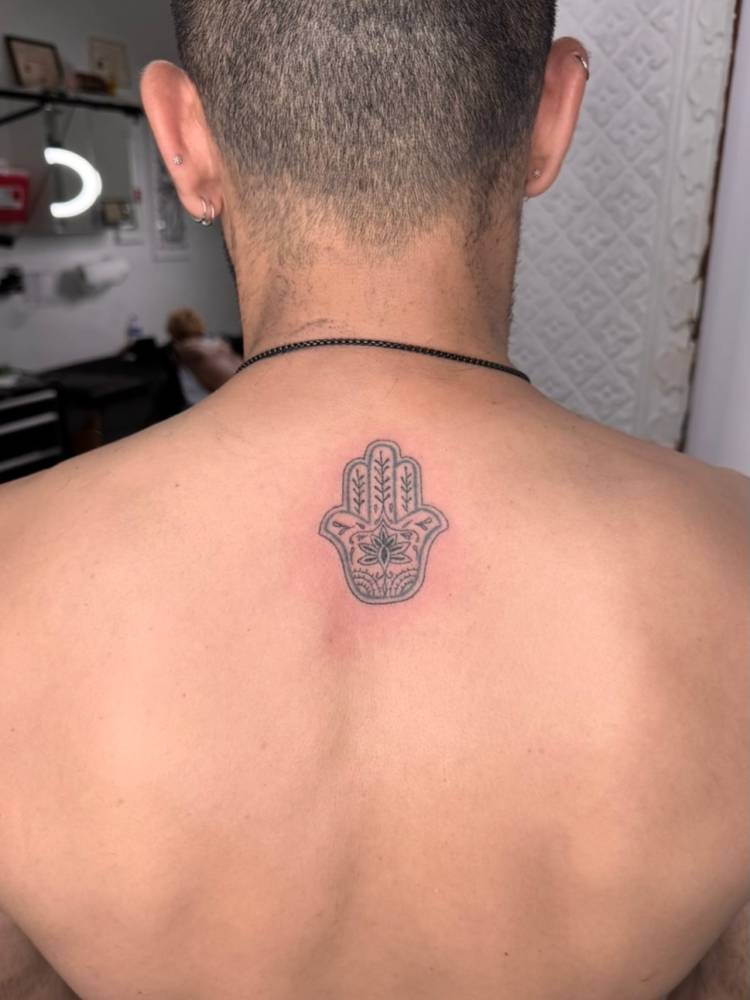 Hamsa tattoo located on the upper back, illustrative style.
