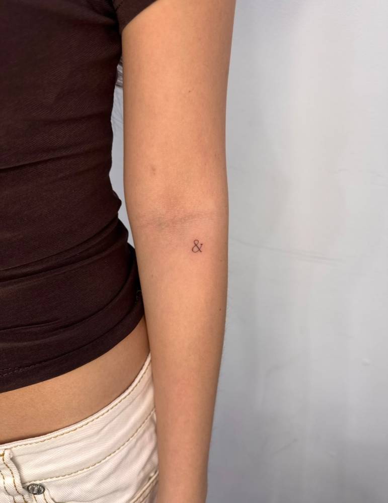 Tiny minimalistic ampersand tattoo placed on the inner forearm.