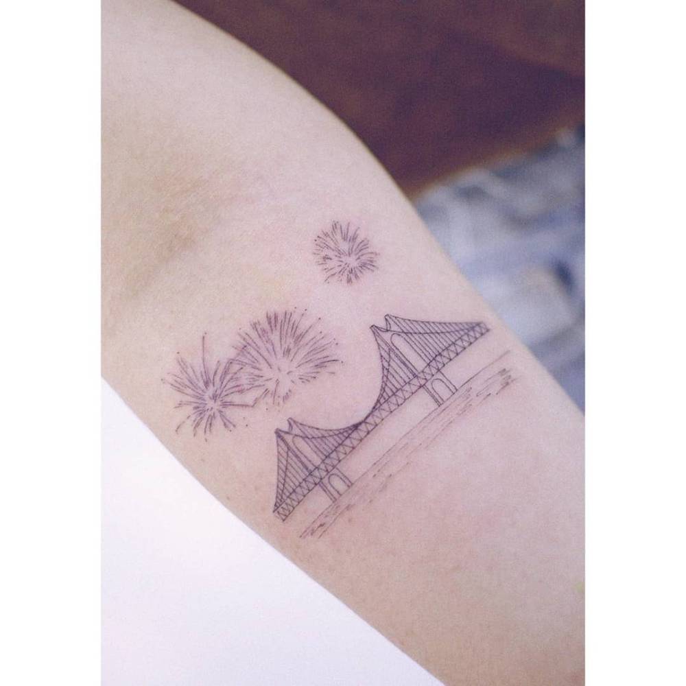 Golden Gate Bridge and fireworks tattoo located on the inner forearm.
