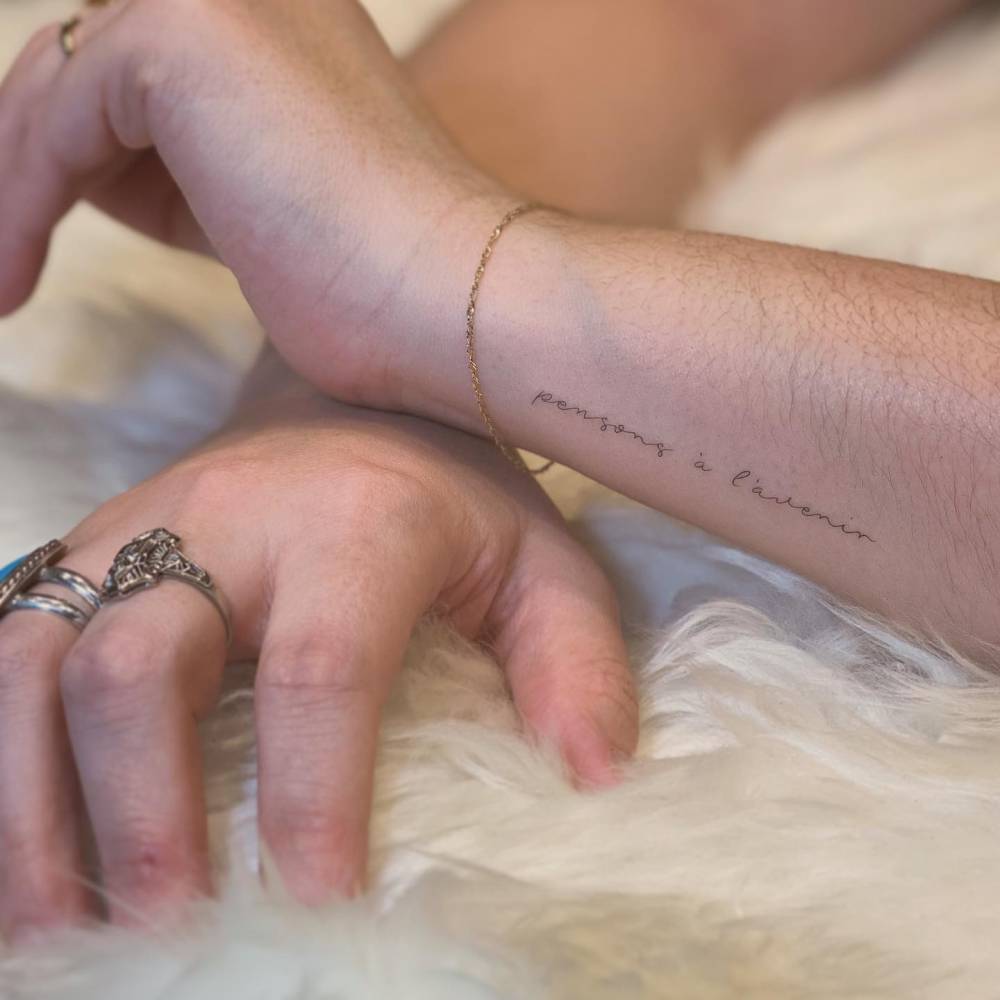 "Pensons a l'avenir" lettering tattoo handwritten on the wrist.