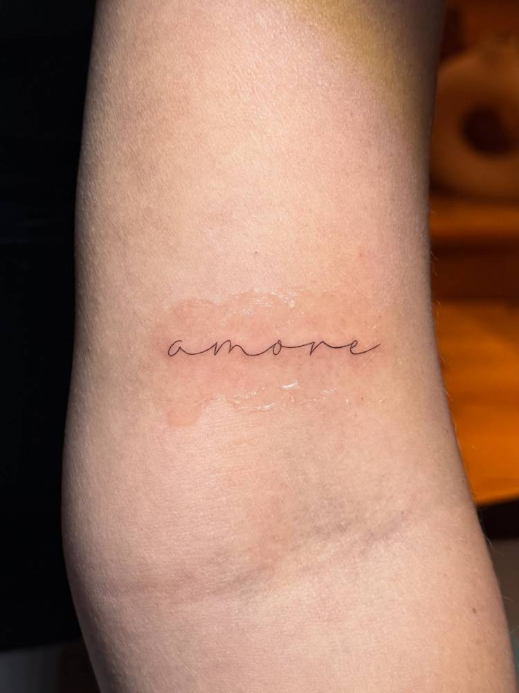 Handwritten font word "amore" tattooed on the bicep.