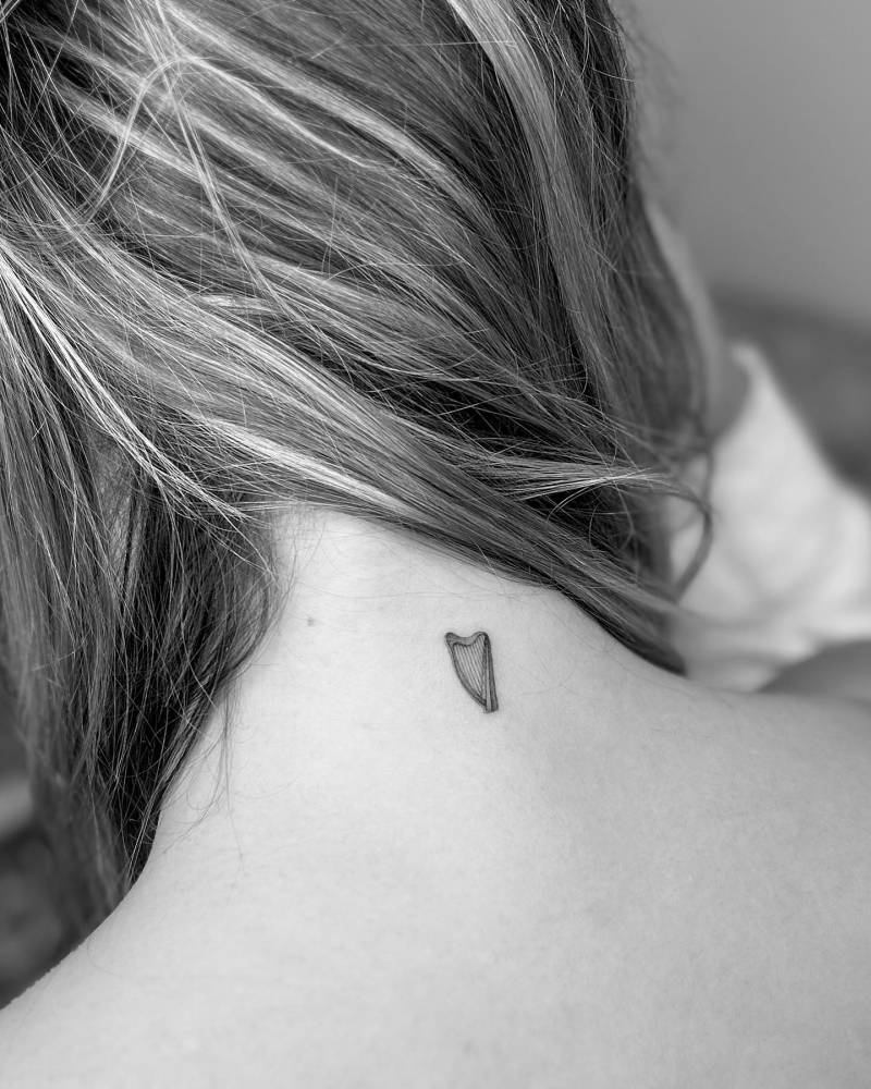 Illustrative style harp tattoo located on the back of the neck.