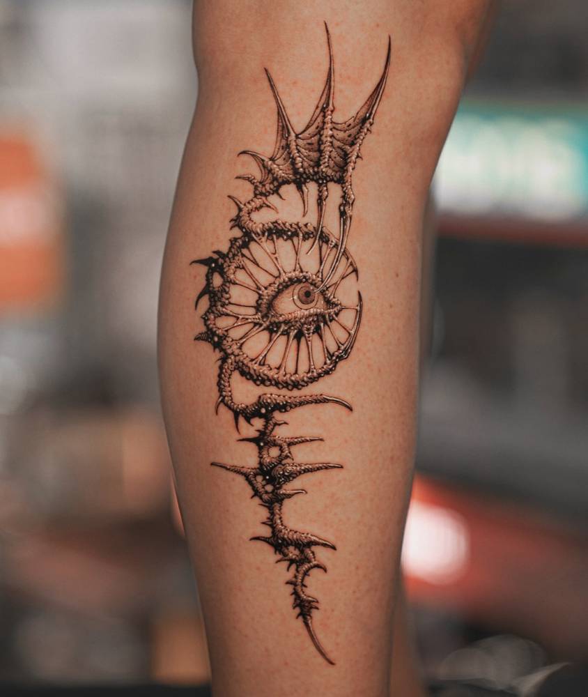 Comic style eye and thorns tattoo located on the shin.