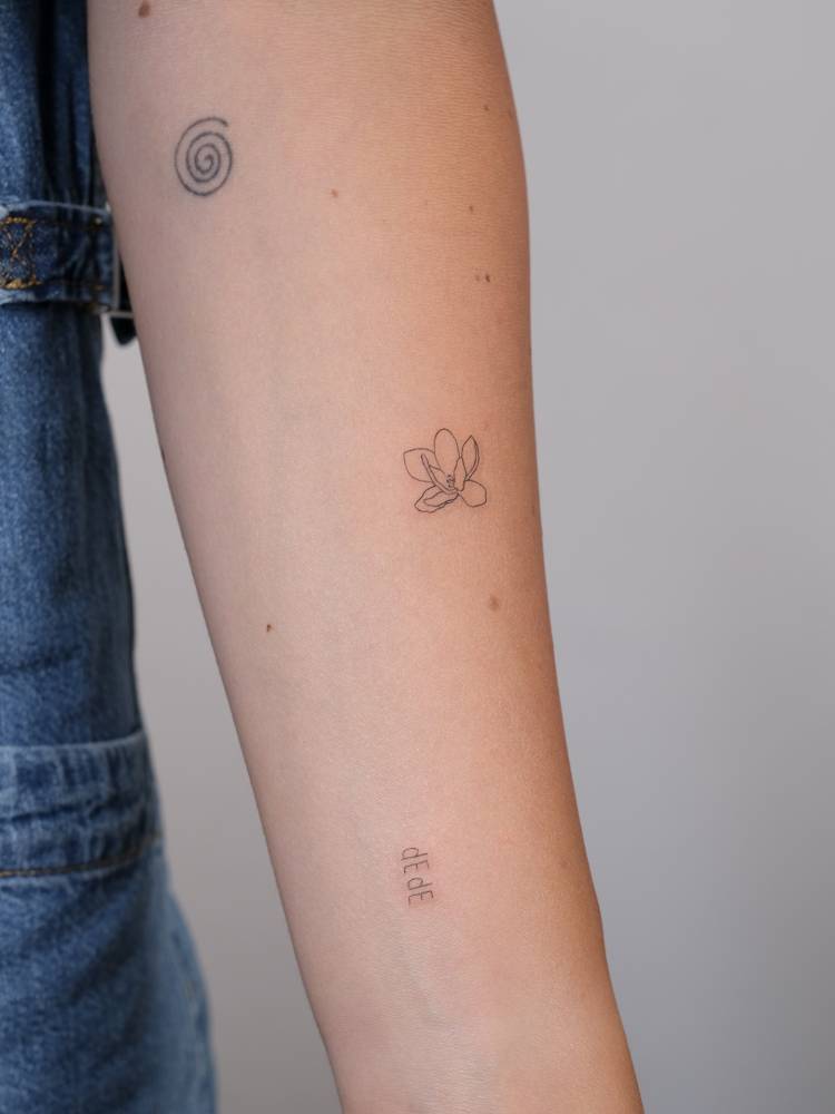 Fine line style magnolia flower tattoo placed on the inner forearm.