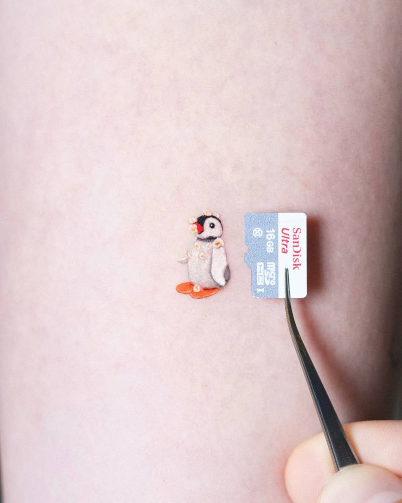 Tiny Pingu tattoo located on the inner forearm, done in cartoon style.