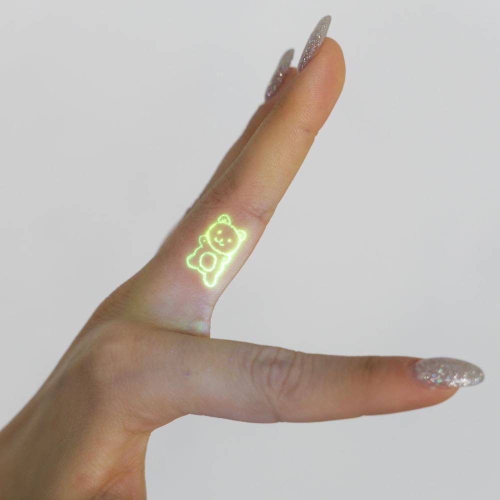 Cute minimalistic bear in UV ink tattooed on the finger.