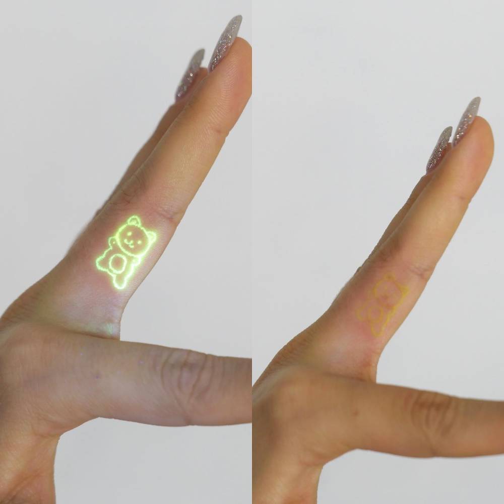 Cute minimalistic bear in UV ink tattooed on the finger.