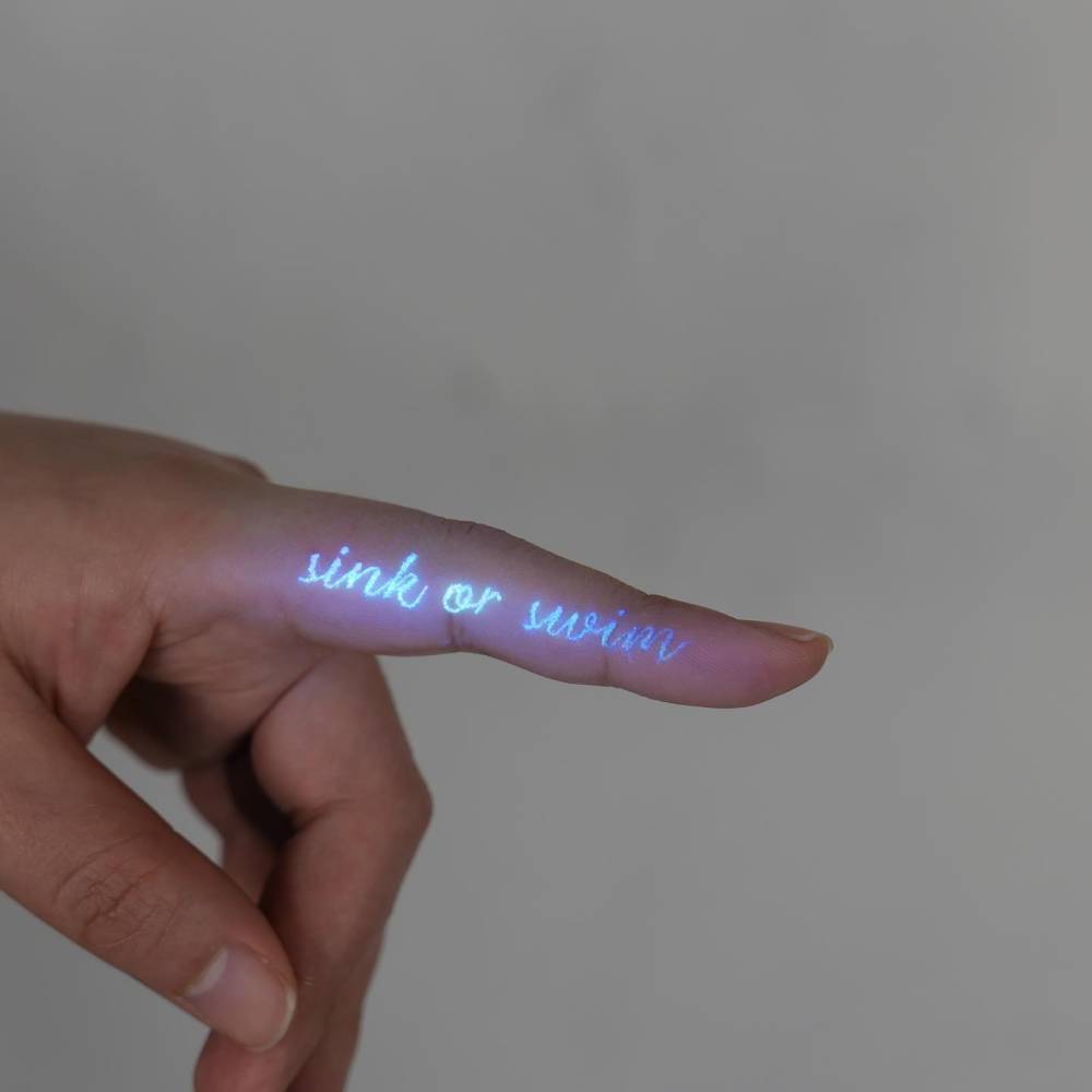 "Sink or swim" lettering tattoo in uv ink located on the finger.