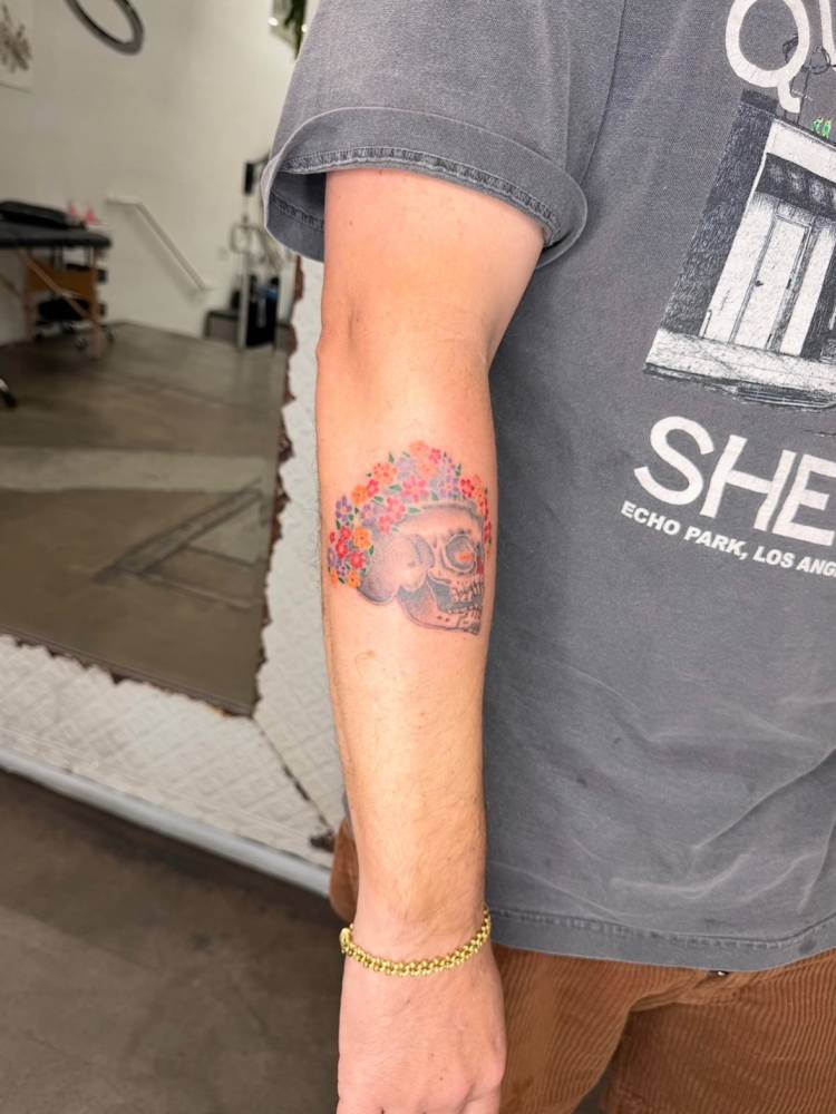 Skull and flowers tattoo in illustrative style placed on the forearm.