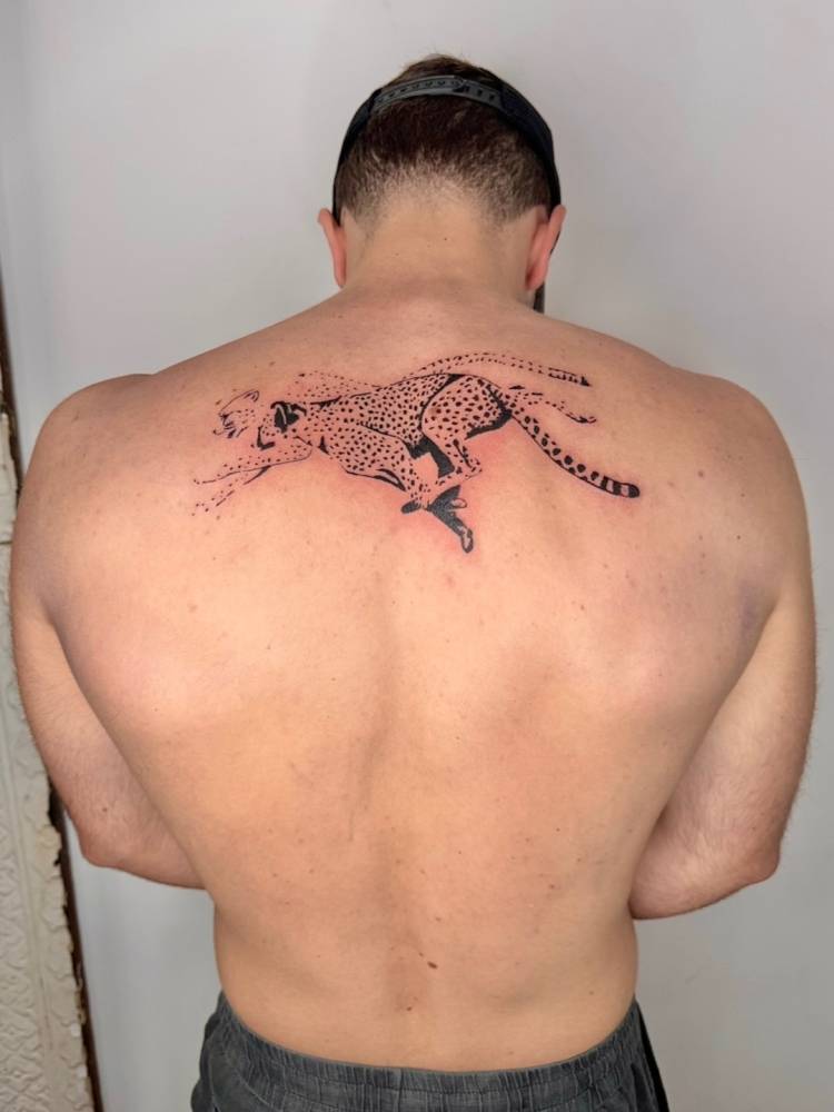 Running cheetah tattoo in black ang grey style placed on the upper back.