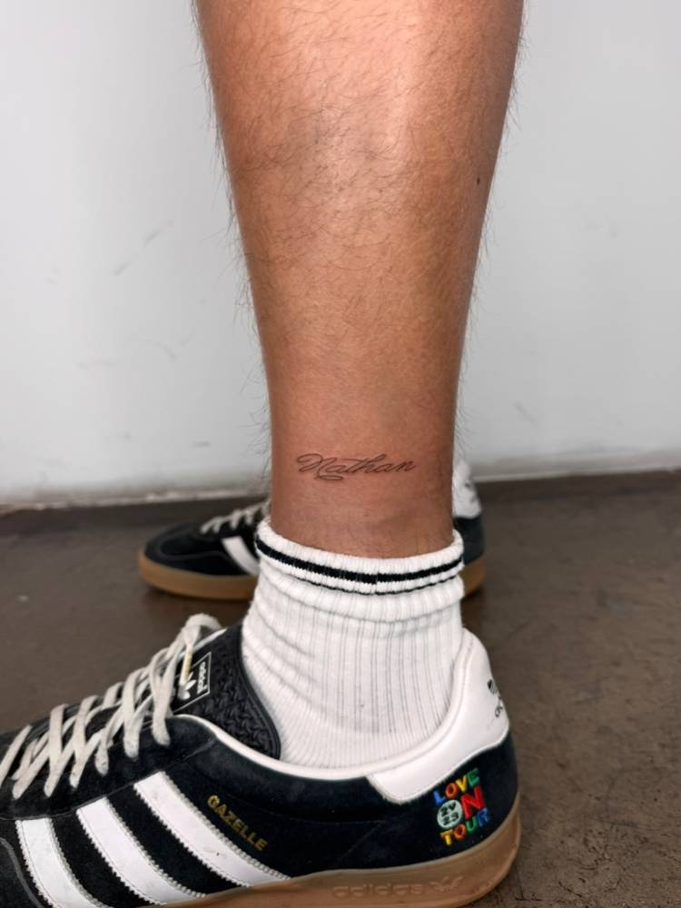 Script font name "Nathan" tattoo located on the shin.
