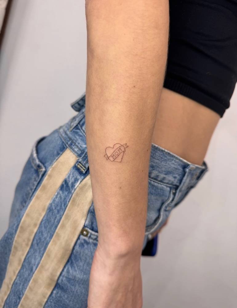 Heart and banner with the word "mom" tattoo located on the forearm.