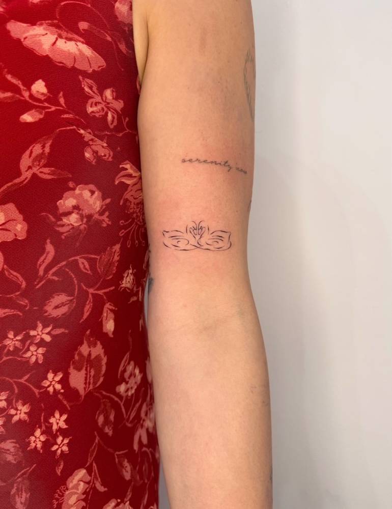 Swan couple tattoo in minimalistic style located on the bicep.