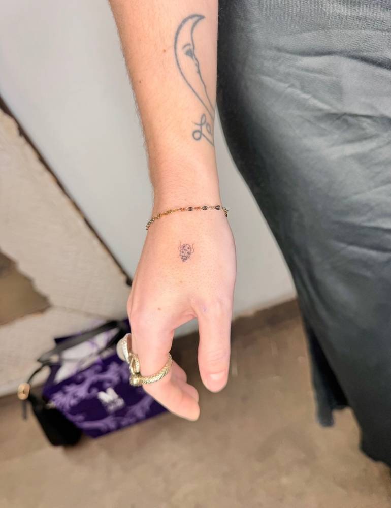 Single needle ladybug tattoo placed on the hand.