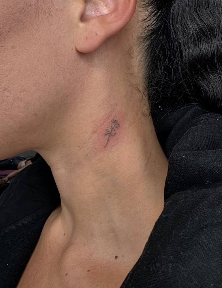 Tiny rose tattoo located on the neck, done in fine line style.