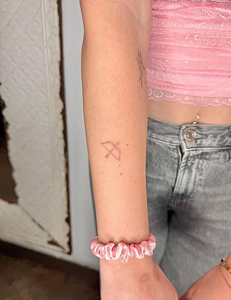 Bow and arrow tattoo in fine line style placed on the forearm.