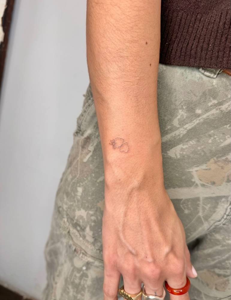 Tiny heart pendant tattoo in fine line style placed on the wrist.