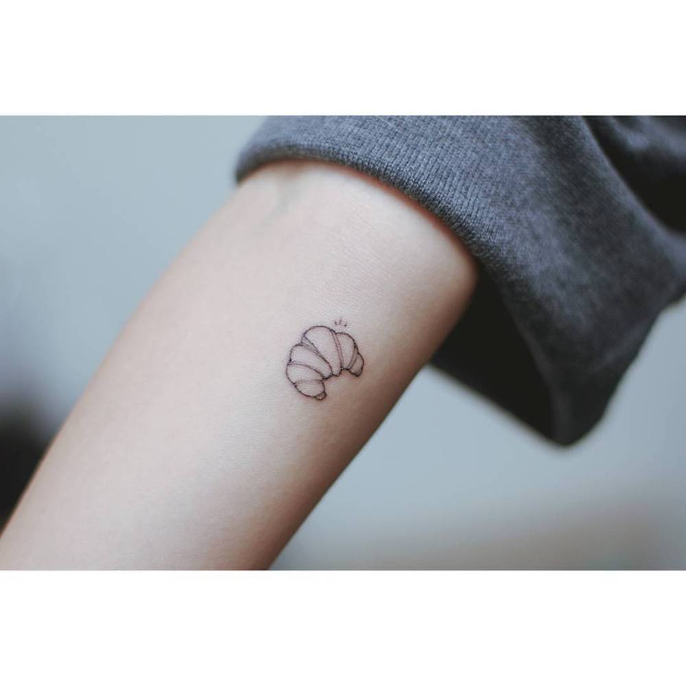 Croissant tattoo located on the inner forearm, fine line style.