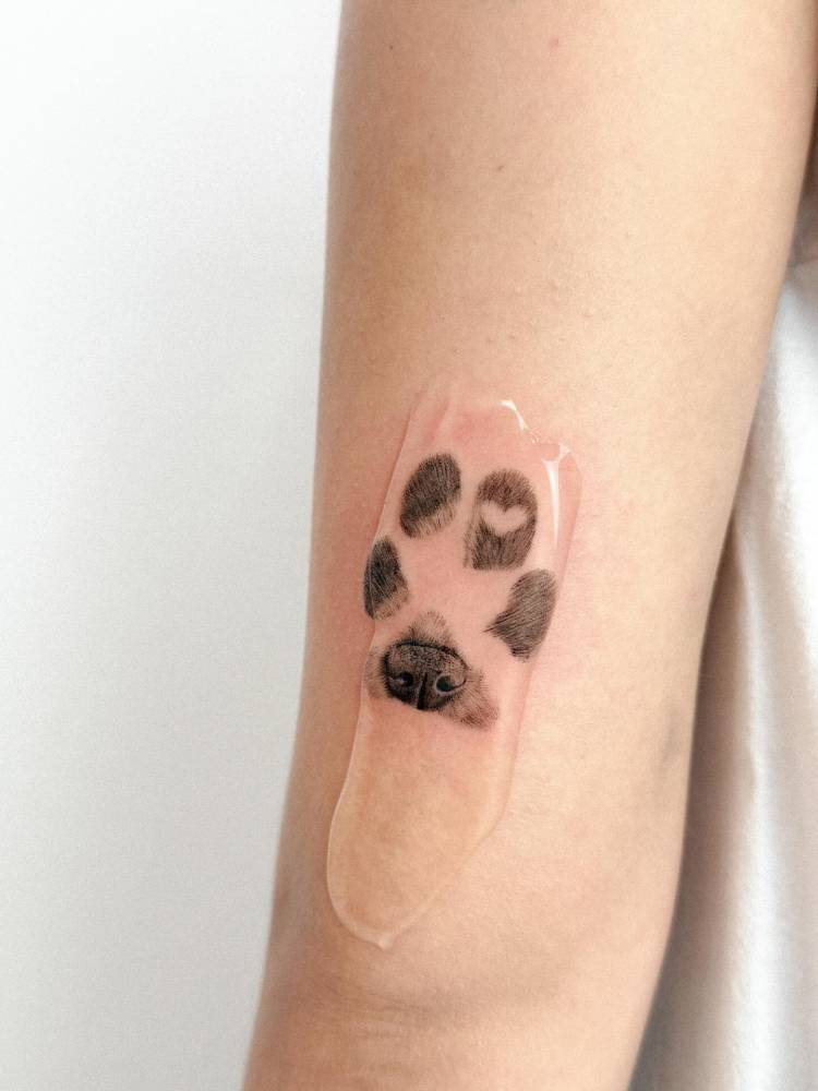 Dog paw print tattoo in watercolor style located on the tricep.