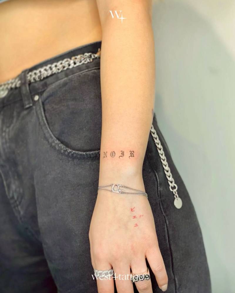 Gothic font word "noir" tattoo located on the wrist.