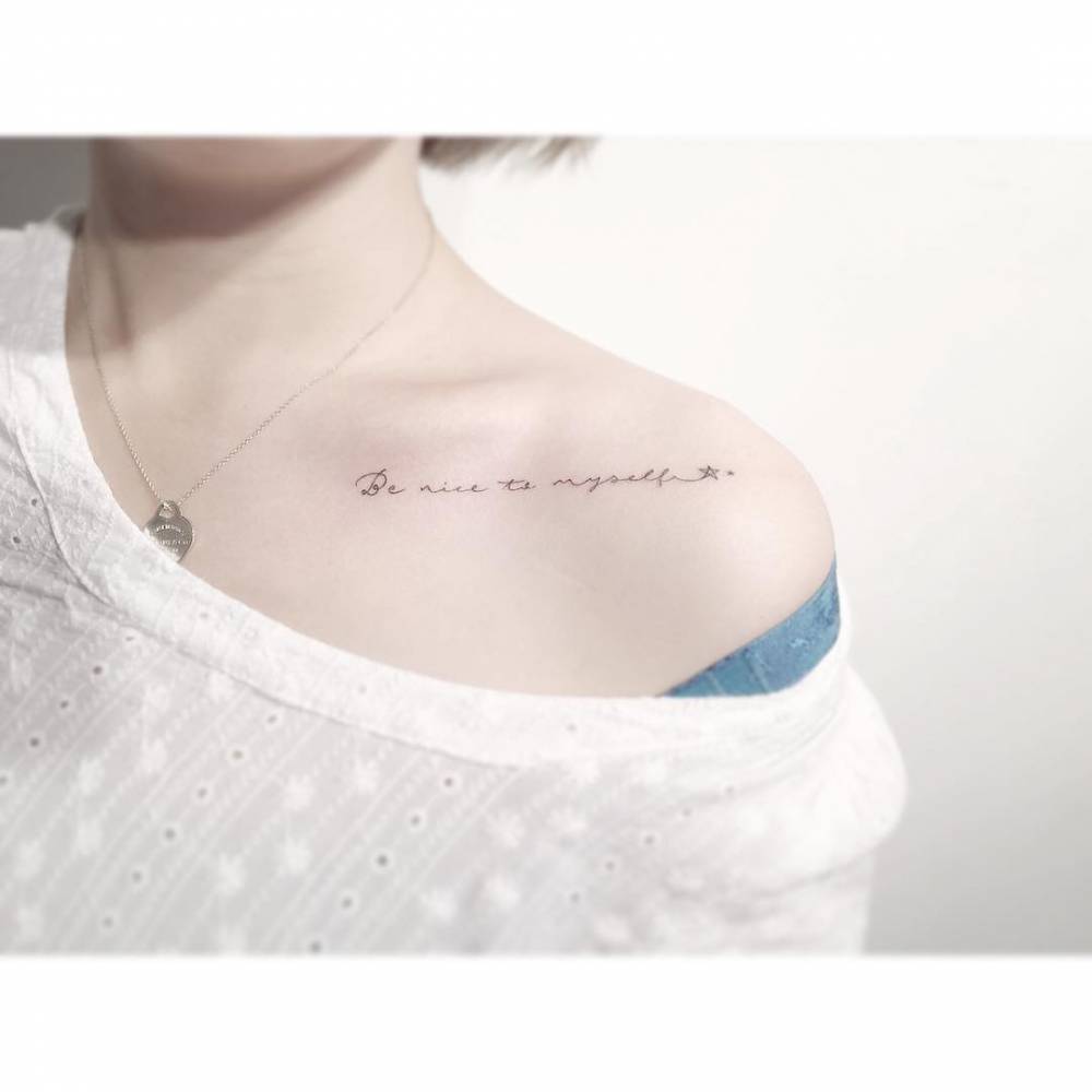 "Be nice to myself" lettering tattoo located on the collarbone.