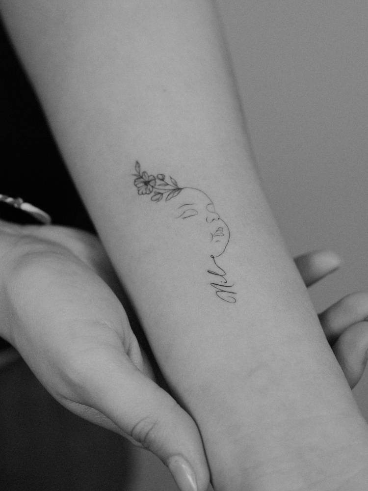Baby portrait tattoo in fine line style located on the inner forearm.