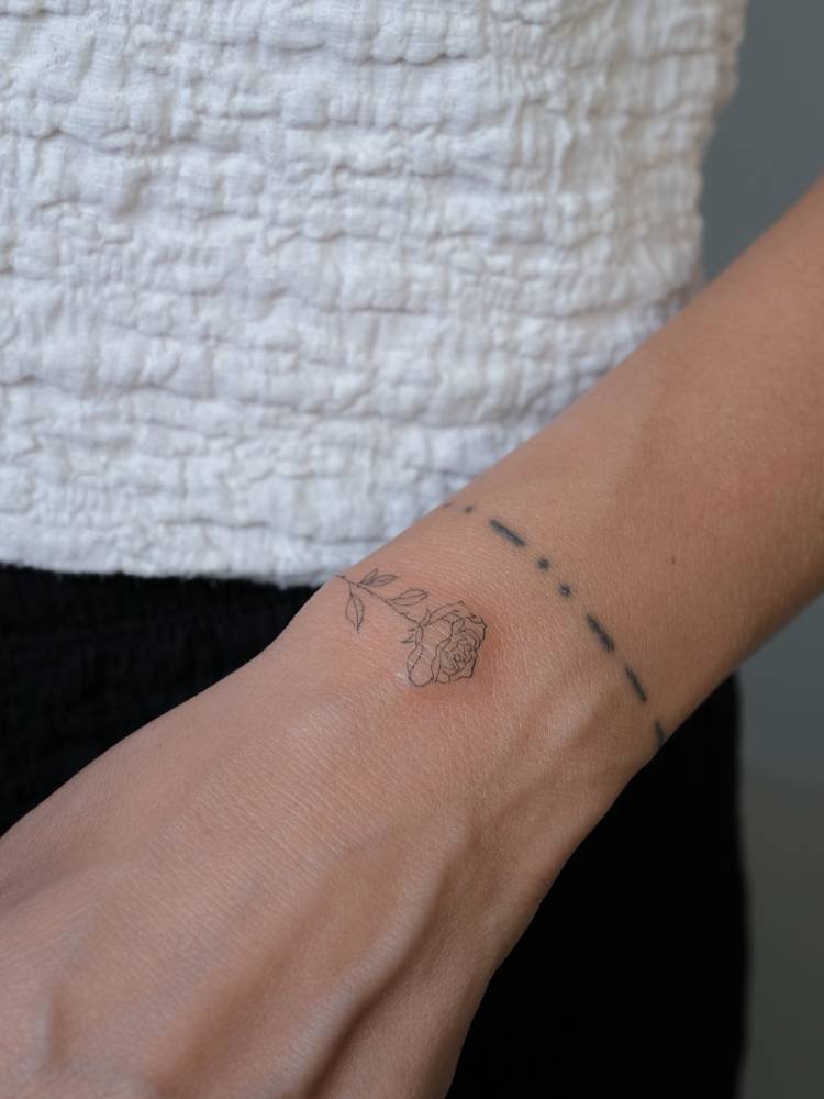 Tiny rose tattoo placed on the wrist, done in fine line style.