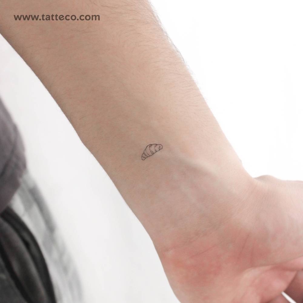 Tiny fine line croissant temporary tattoo located on the wrist.