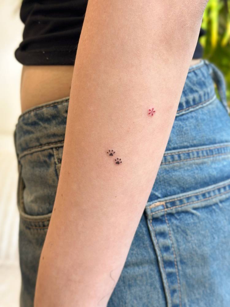 Tiny paw prints and red flower tattooed on the forearm, minimalistic style.