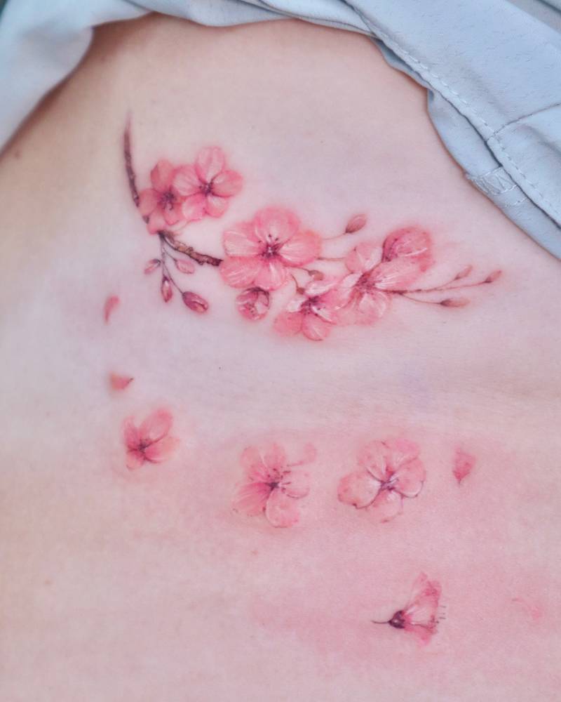 Watercolor style cherry blossom tattoo located on the rib.