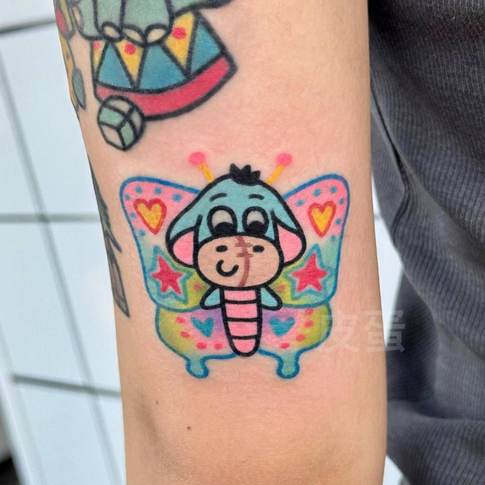 Eeyore butterfly tattoo located on the tricep, cartoon style.
