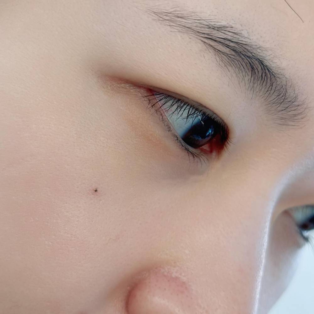 Tiny minimalistic dot tattoo located on the face.